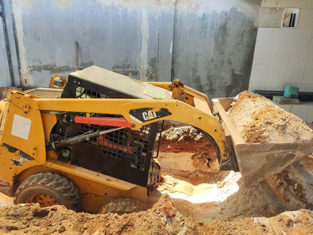 Minicarregadeira retirando piso e terra numa demolição em área interna