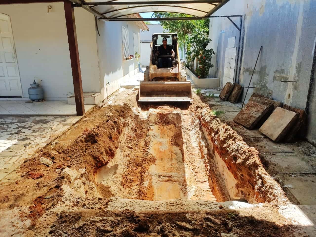 Minicarregadeira de pneus abrindo uma vala comprida no corredor de uma casa