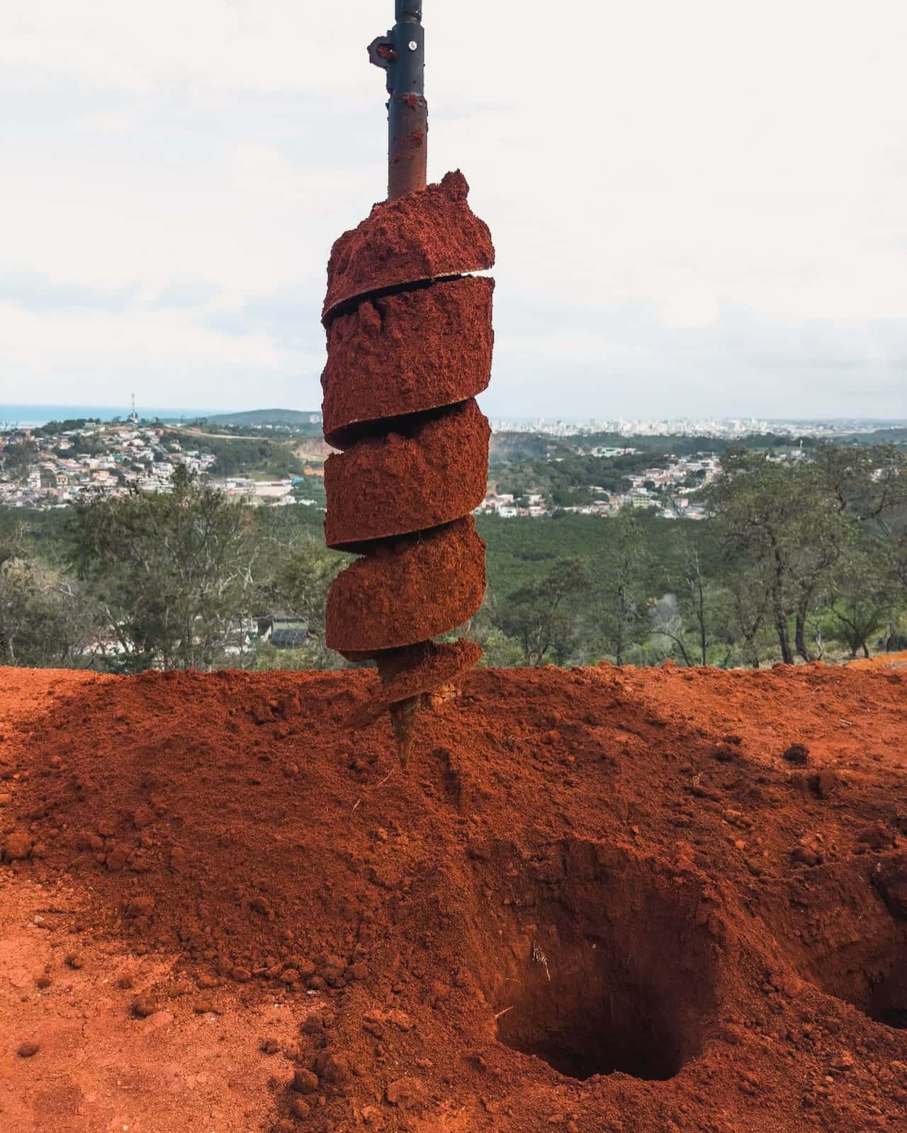 Broca de perfuração de solo saindo do buraco, com a cidade ao fundo